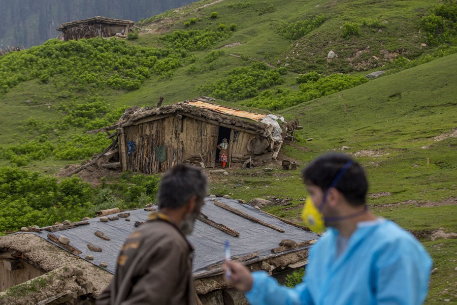 A health-care worker interacts with shepherds in a remote settlement on a hillside.