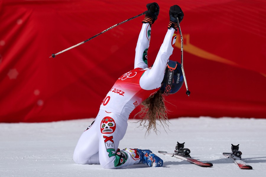 A skier raises her arms and celebrates, on her knees, after a run.