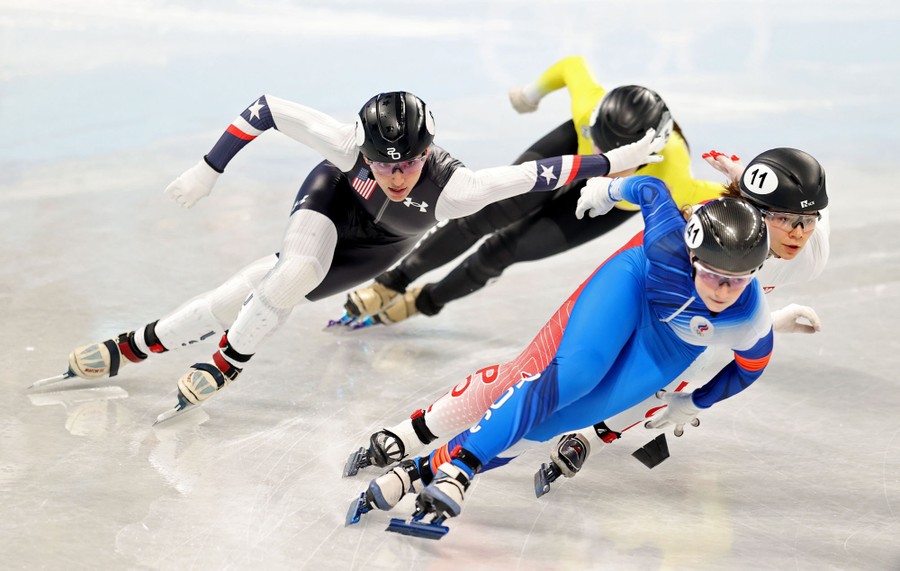 Four racing speed skaters lean sharply into a turn.