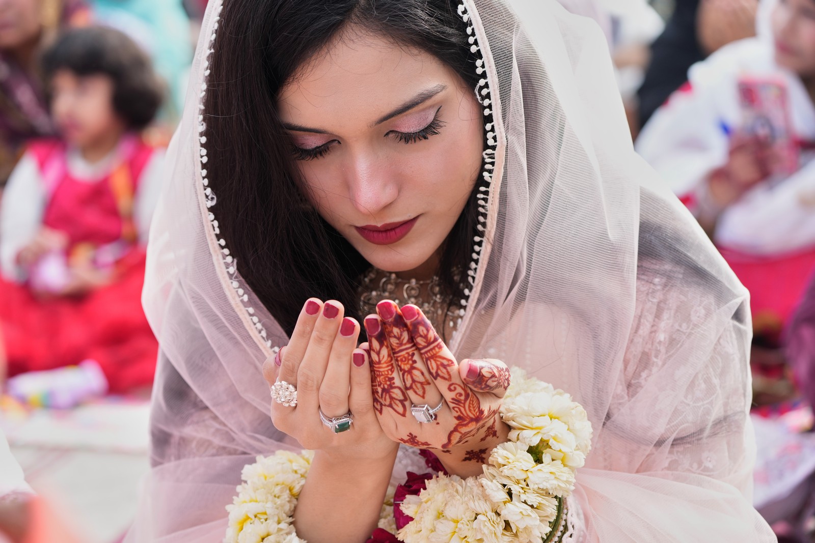A woman leans over while praying, with henna decorations on her hand.
