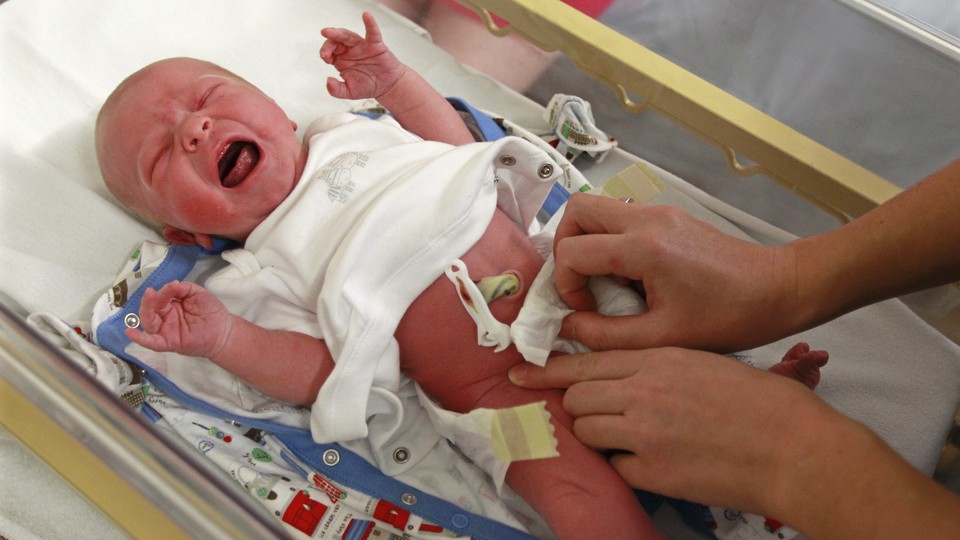 A crying baby is examined in a hospital crib.