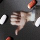 A hand making a thumbs-up and a hand making a thumbs-down behind a field of Paxlovid pills