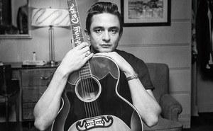 photo of Johnny Cash resting his chin on and holding a guitar with his name on the neck
