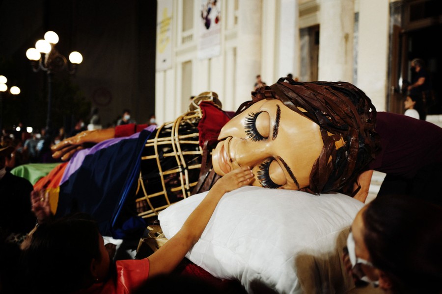A giant puppet "sleeps," laying down outside a theater at night.