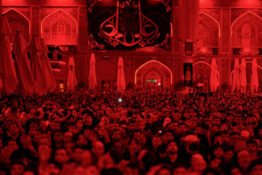 Ένα μεγάλο πλήθος συγκεντρώνεται μέσα σε ένα ιερό, που φωτίζεται από κόκκινο φως.