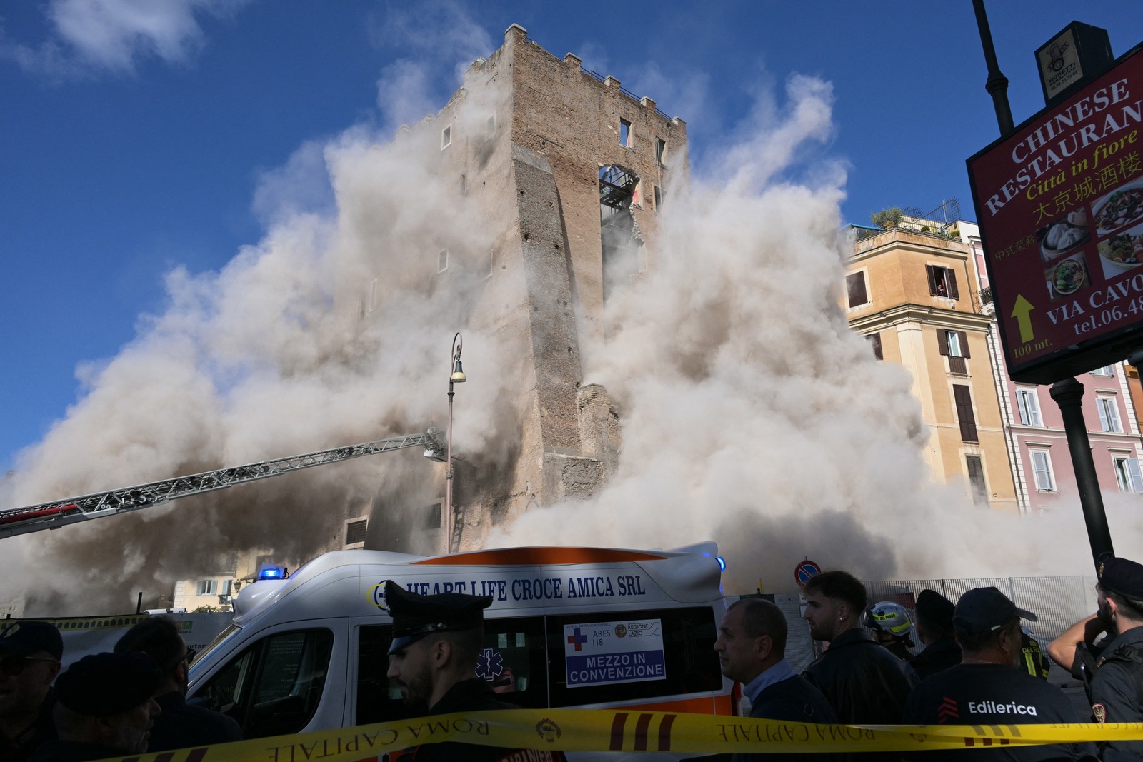 Dust rises around a historic building that is partially collapsing.