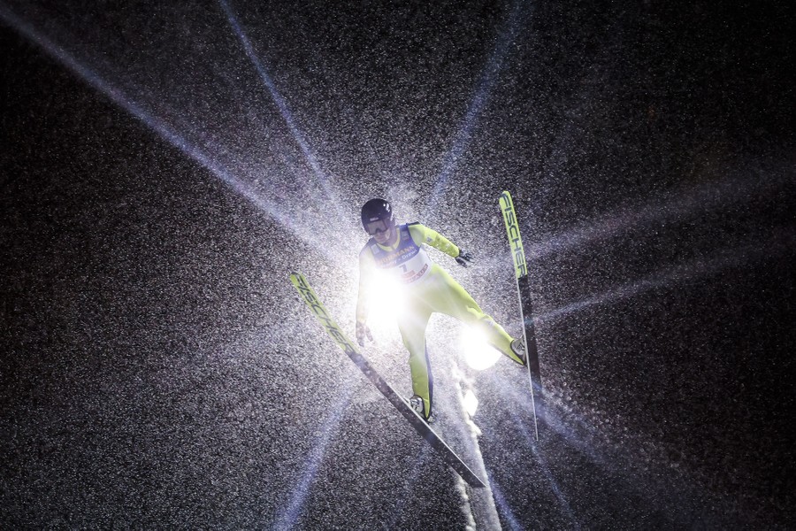 A ski jumper in mid-air, seen during a snowstorm, with a bright light behind them