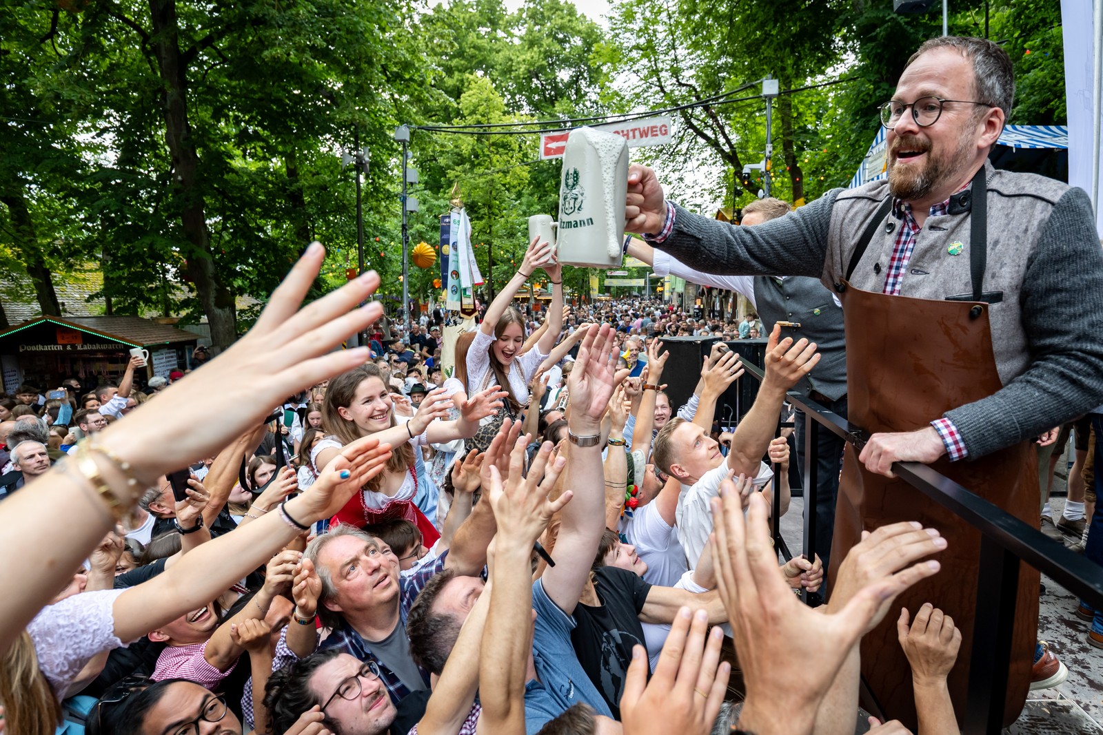 A man holds a full beer mug above a crowd of eager festival-goers, who reach up for it.