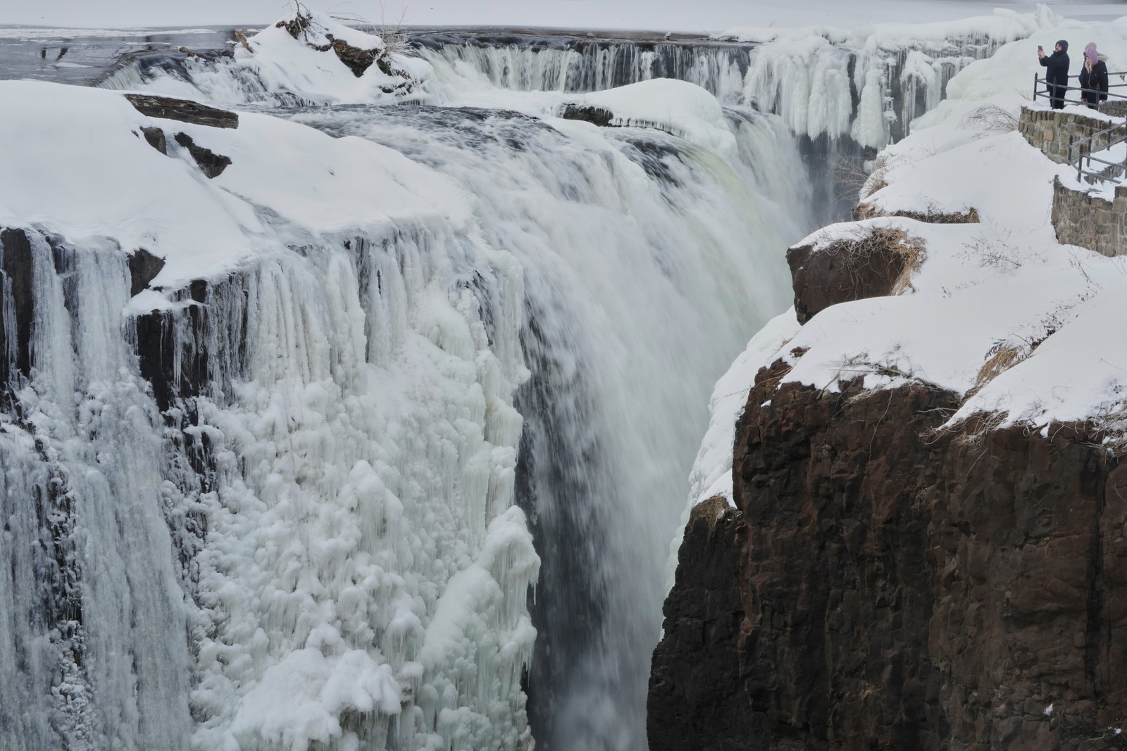 People look over a partially-frozen waterfall.