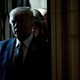 A 2017 photo of then-President Donald Trump wearing a blue suit and tie, standing in a dark corridor