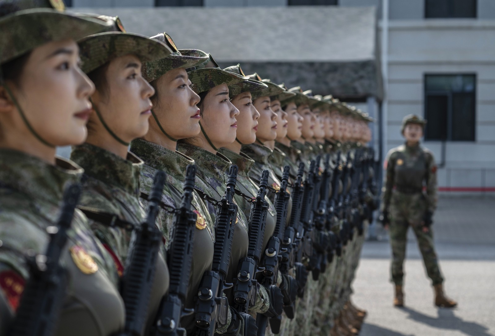 Female soldiers stand side-by-side in close formation, seen from the side.