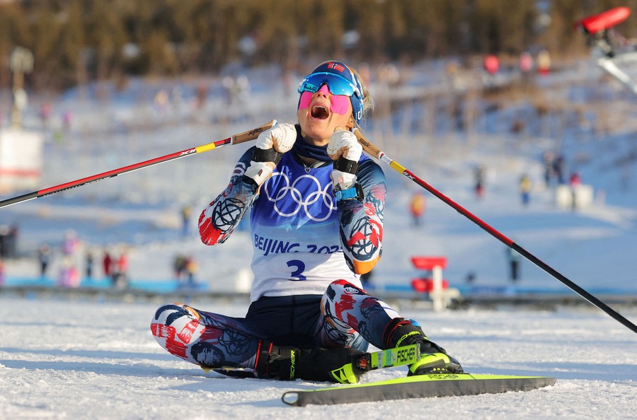 A skier celebrates while sitting on snow after a race.