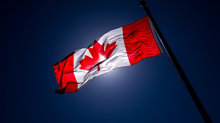 A Canadian flag, slightly darkened by the light, waves in the air.