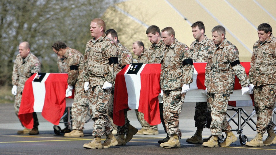 The coffins of two Danish soldiers who were killed in Afghanistan are draped in Danish flags and carried out of a military transport plane in Denmark by men in military uniforms.