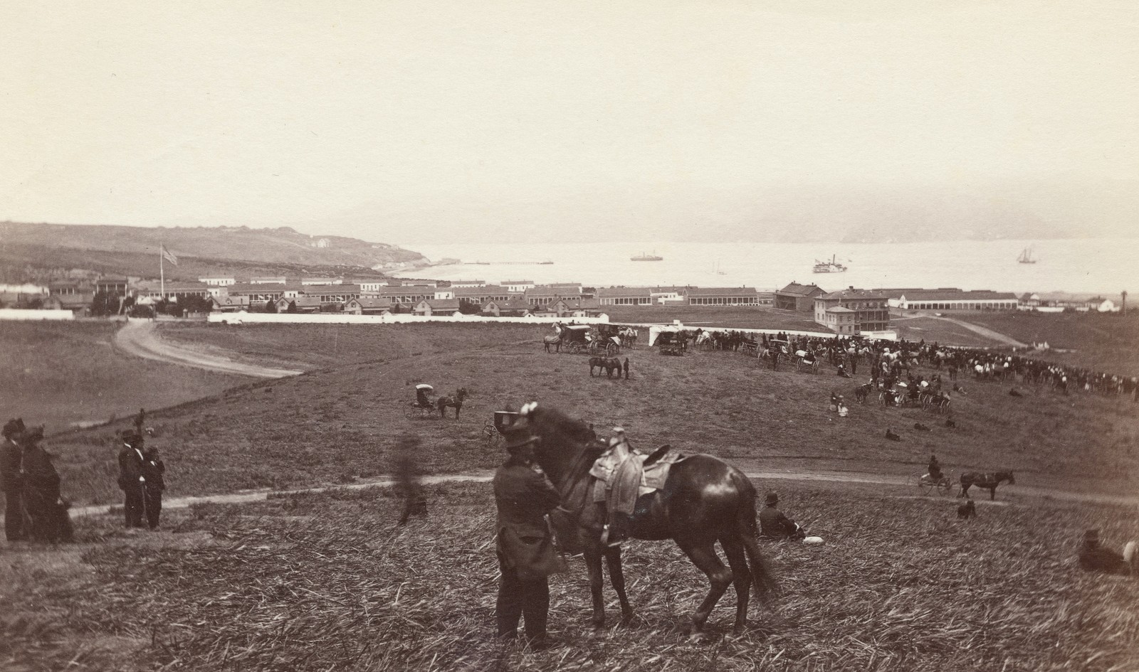 An overview of visitors with their horses and carriages, gathering in a hillside field with a view of San Francisco Bay.