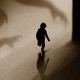 Photo illustration of a child running from shadowy hands.