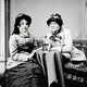 A black-and-white photo of two 19th-century women sitting at a table with a bottle of whiskey and a cigar