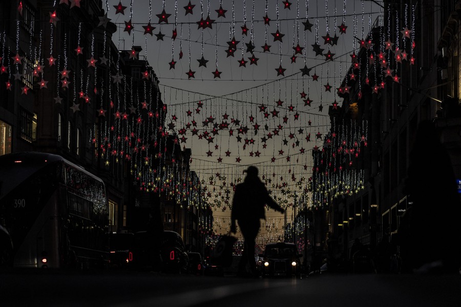 People walk and drive ina street decorated with hundreds of red lit stars hanging from lines across the road.