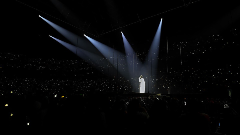 Suga sings in a dark arena, with five spotlights on him.
