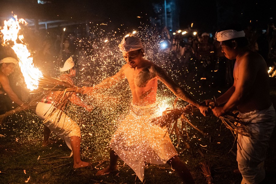 Several men strike other men in a plaza with burning coconut leaves, sending sparks flying in the air.