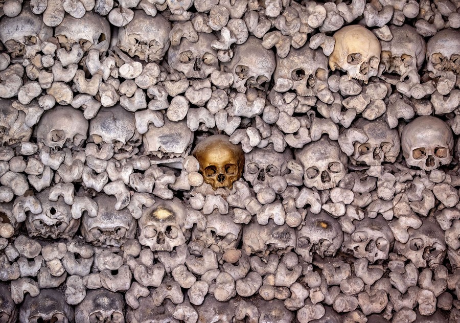 A single gold skull sits embedded in a large wall made up of skulls and bones.