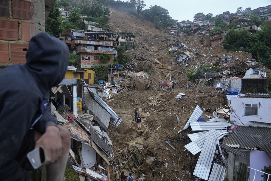 People move about amid landslide debris in a steep ravine among houses.