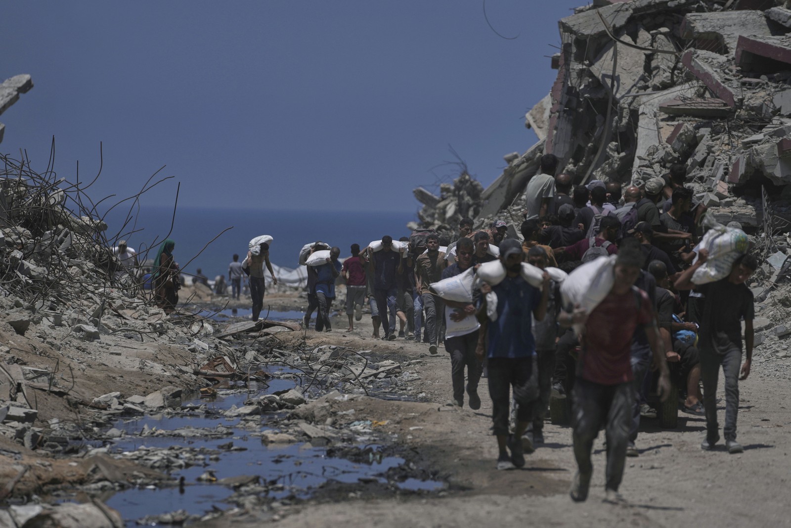 Many people carry sacks of flour past the ruins of destroyed building buildings.