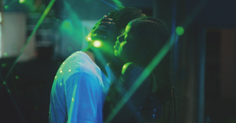 Image is from the film 'Atlantics' (2019). Two people dance in an embrace. They are surrounded by green lasers, which highlight their faces in the darkness.