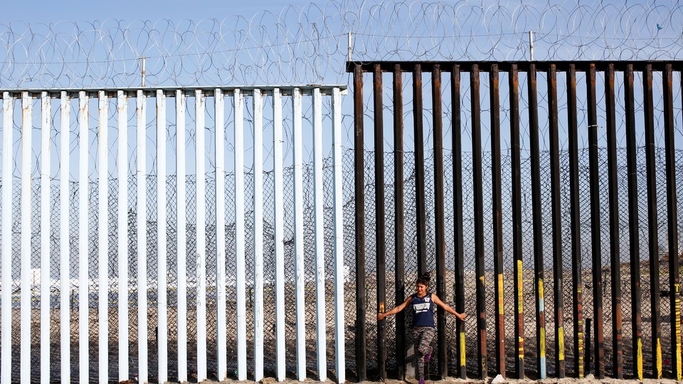 A woman leans against the U.S.-Mexico border wall