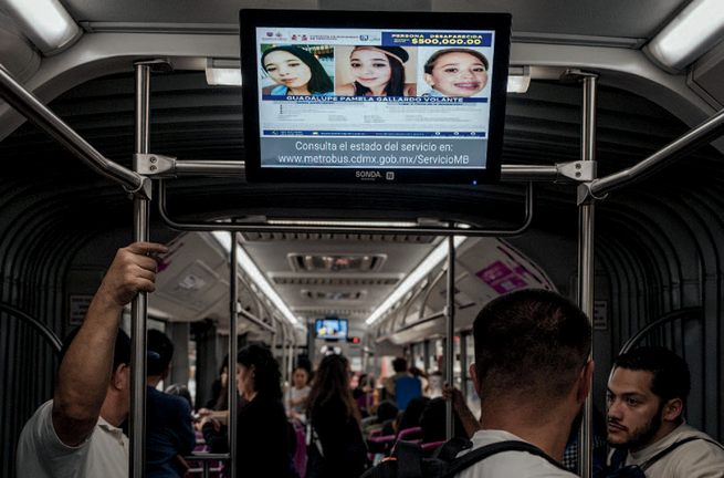 the inside of a bus in Mexico City, with the faces of three missing people displayed on a small TV screen