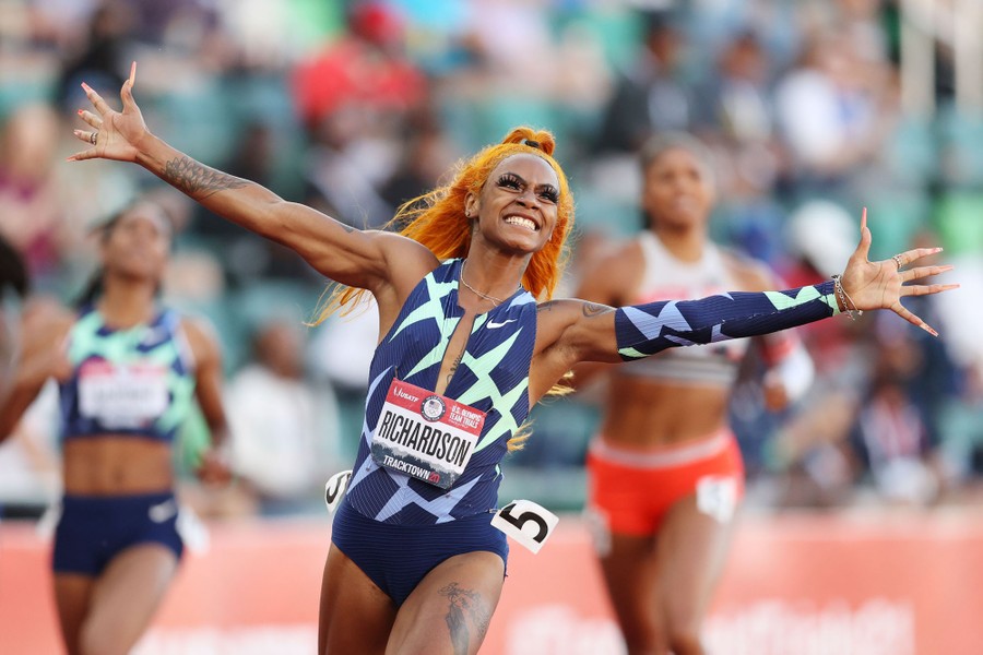 An athlete runs while smiling and holding her arms wide after winning a race.