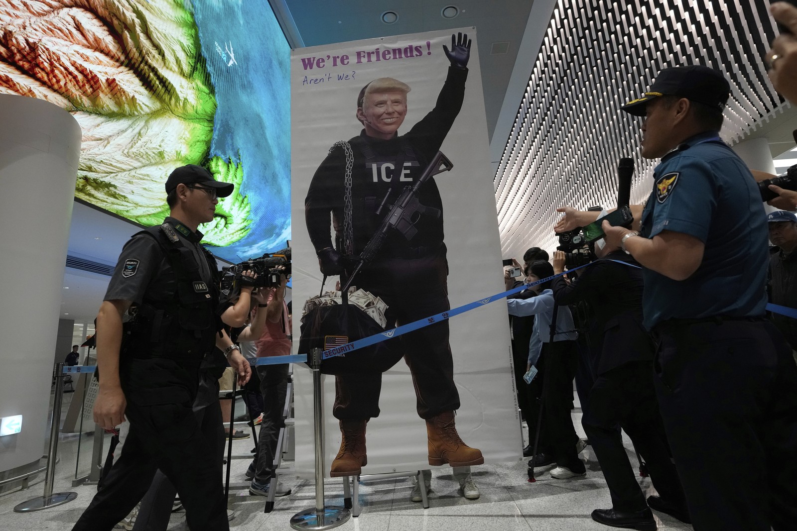 Security officers in a Korean airport walk past a protest banner depicting President Trump wearing an ICE uniform.
