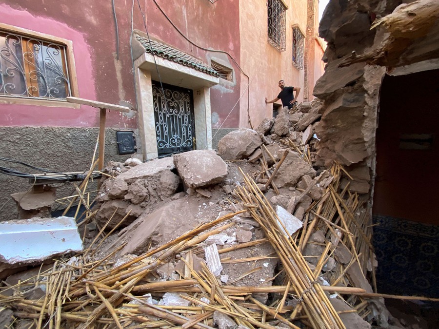 A person stands in a narrow street that is full of earthquake rubble.