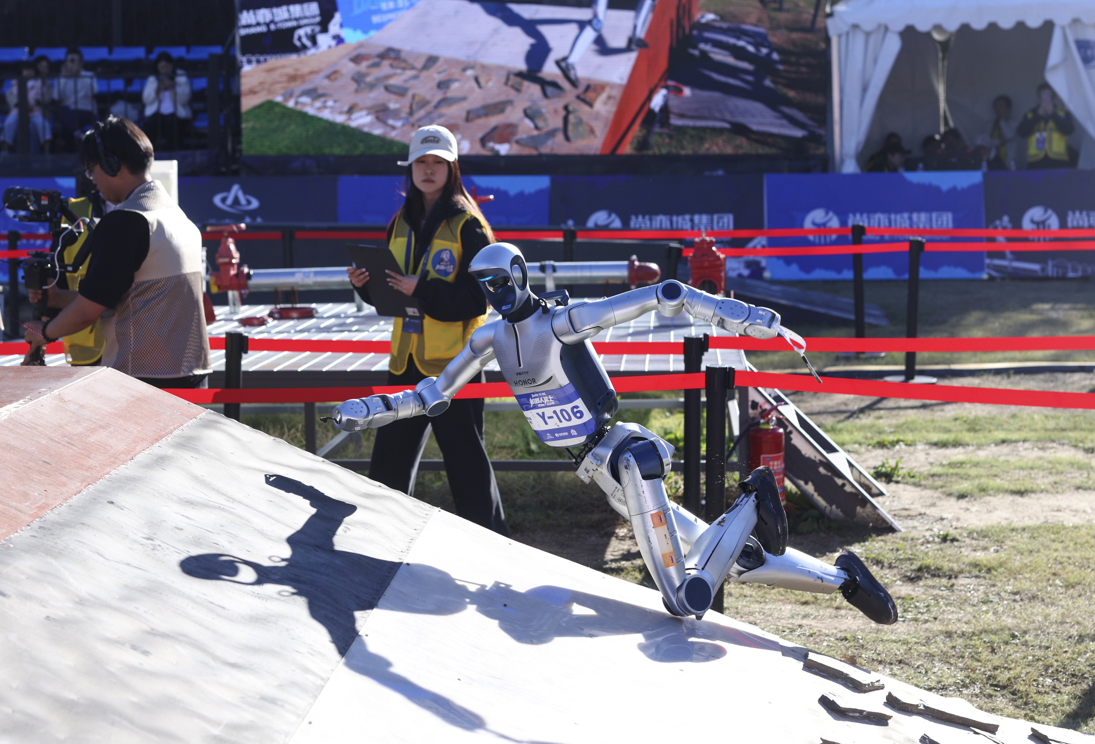 A humanoid robot competitor falls while navigating a slope obstacle.