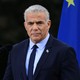 Yair Lapid, wearing a navy suit and tie, stands in front of a pair of microphones, with the EU flag in the background.