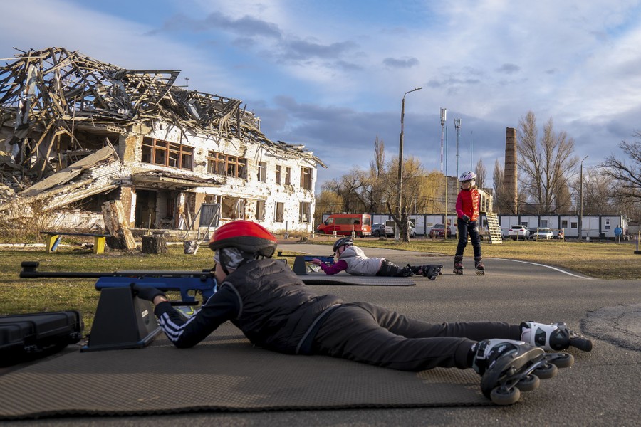 Children wearing roller blades practice shooting with rifles while lying prone.