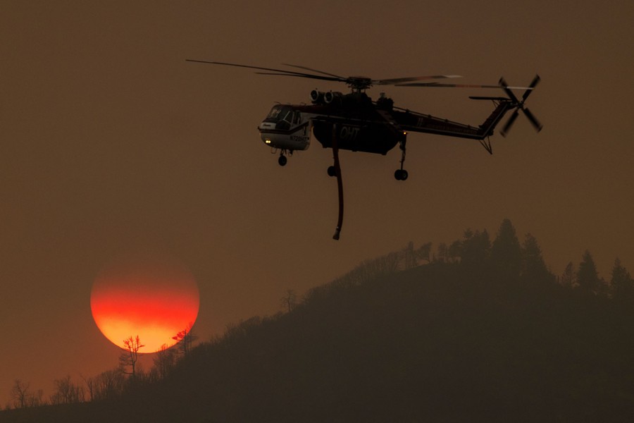 A firefighting helicopter passes in front of the setting sun.