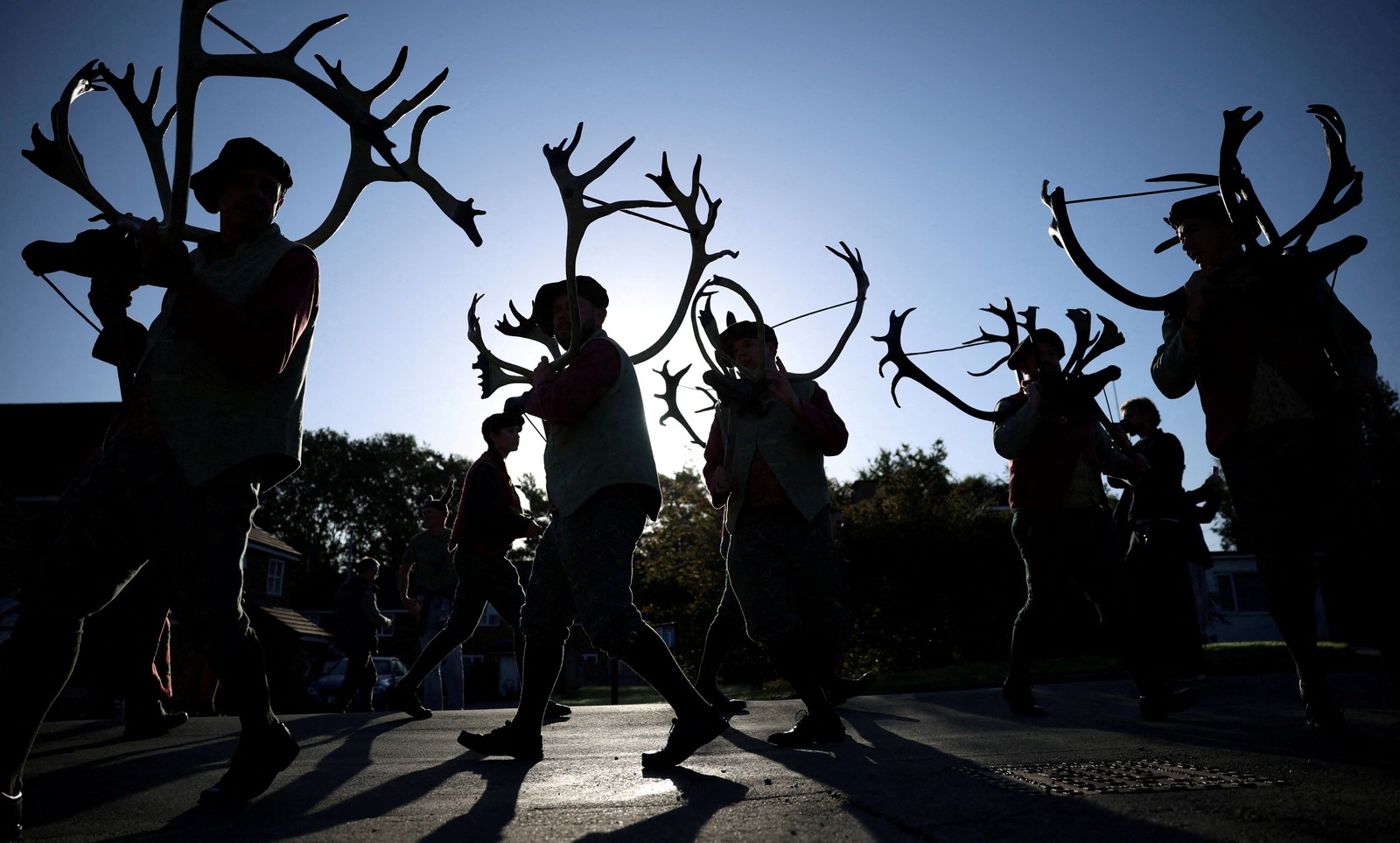 Performers walk along a road while carrying large sets of antlers each.