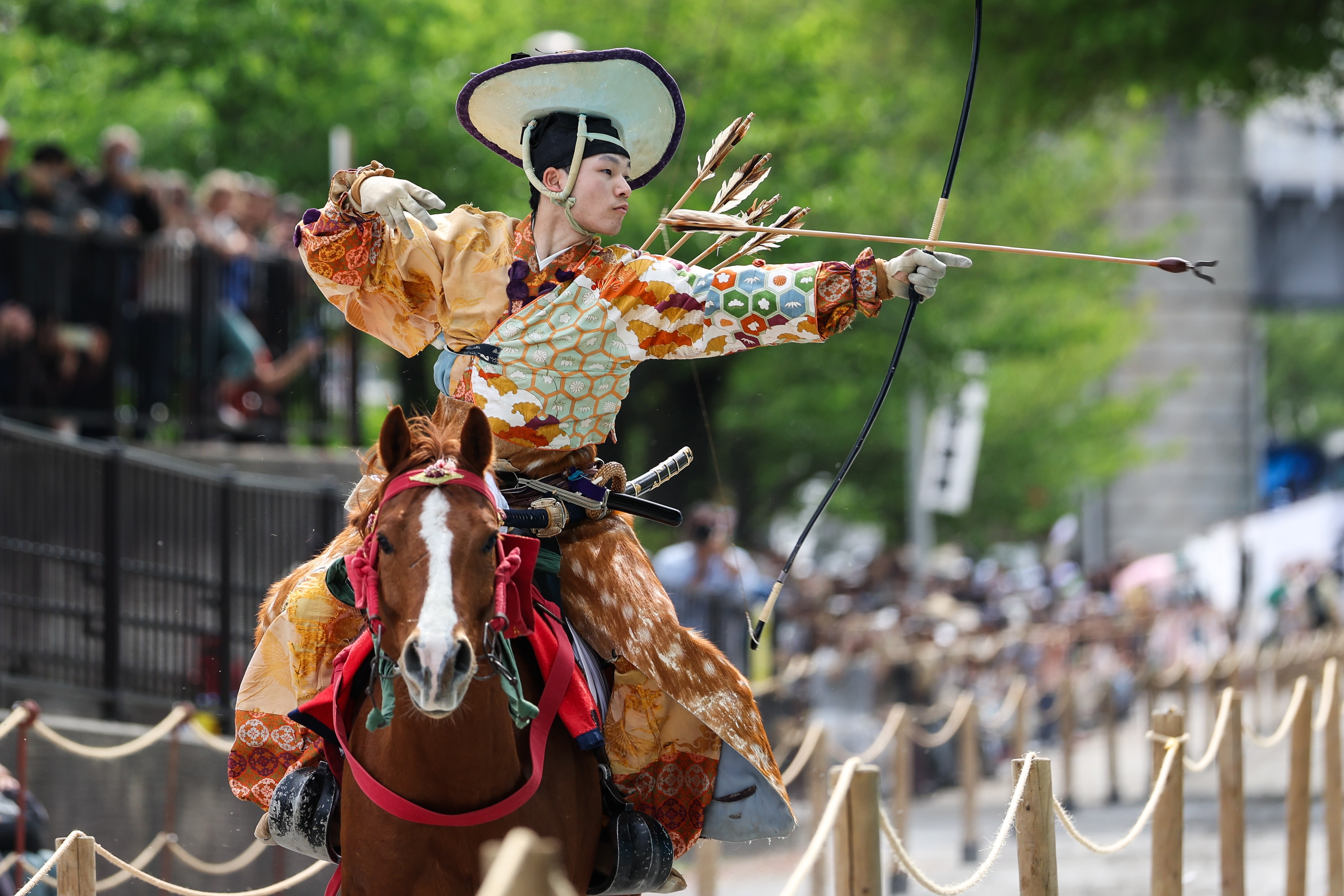 An archer on horseback, wearing traditional Japanese clothing, shoots an arrow at a target