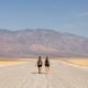 Two hikers walk on a path in front of barren mountains