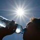 A photograph of a woman drinking from a water bottle, with a full afternoon sun blazing onto her.