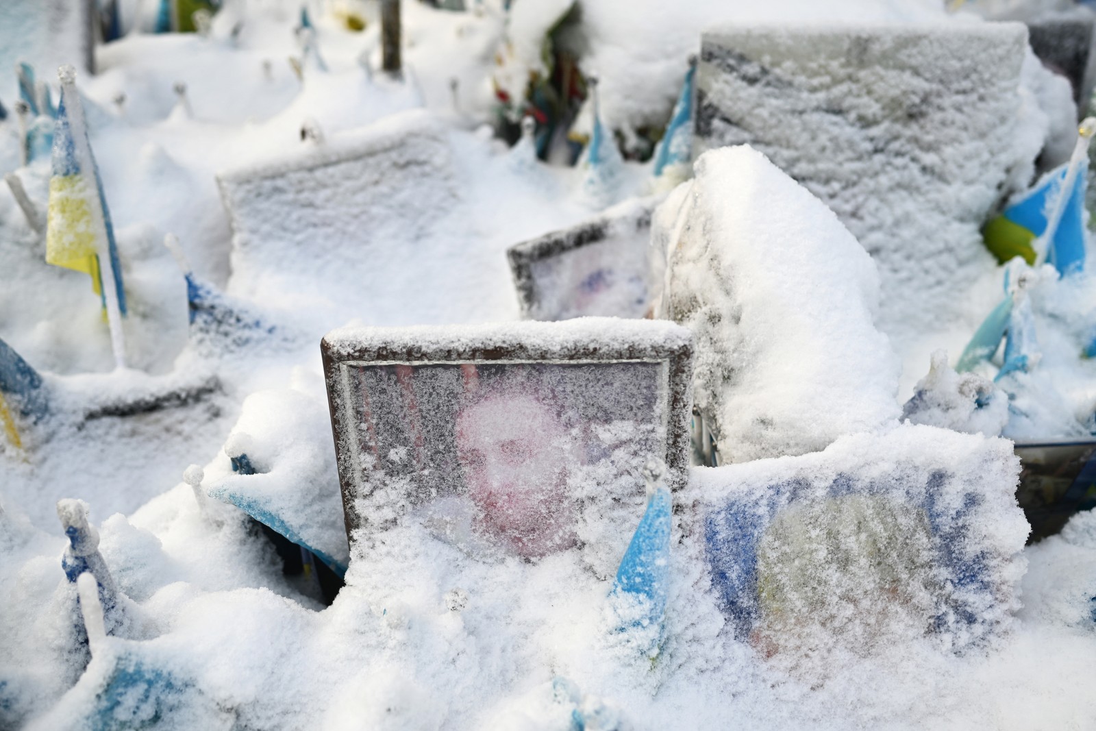 Portraits of fallen Ukrainian fighters sit in a memorial, covered by recent snowfall.