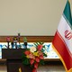 A color photograph of Iranian and Russian flags flanking a podium mounted with several microphones.