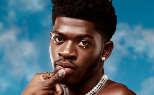 Lil Nas X shirtless in bedazzled jewelry against a blue sky