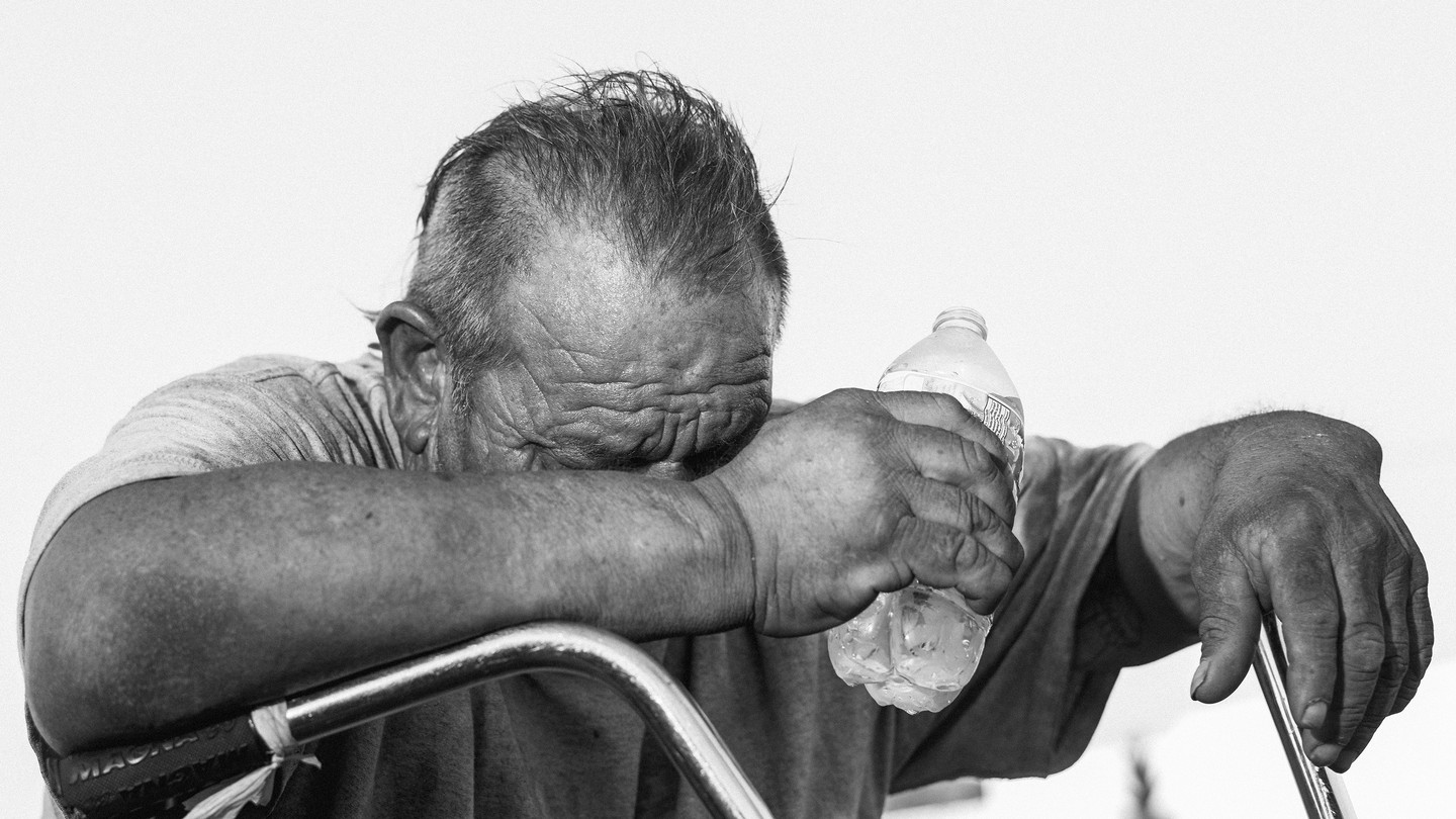 A man holding his head down, grasping a water bottle