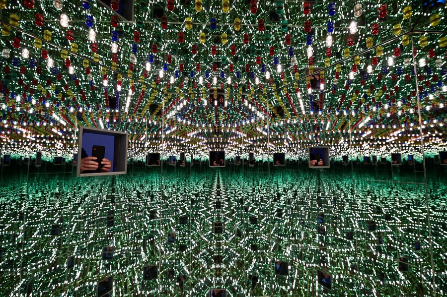 A person takes a photograph of the interior of a mirrored art exhibit.