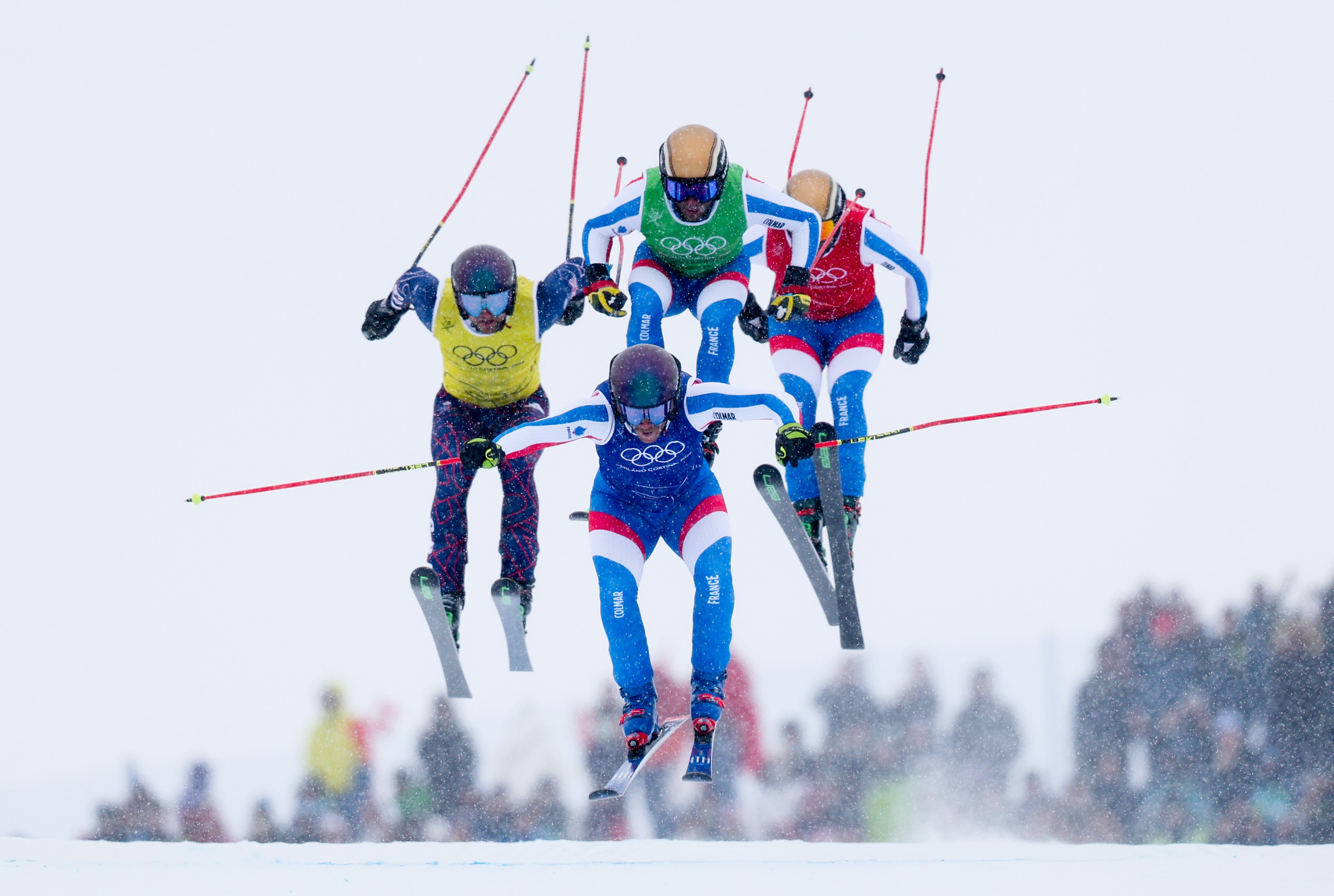 Four ski racers, seen in midair, jumping during a race