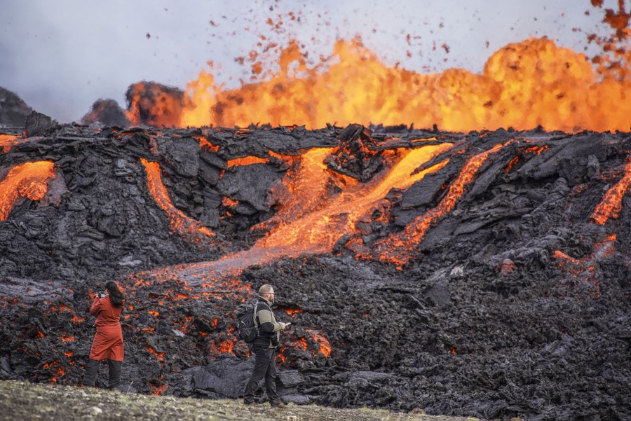 Two people walk in front of a large lava flow.