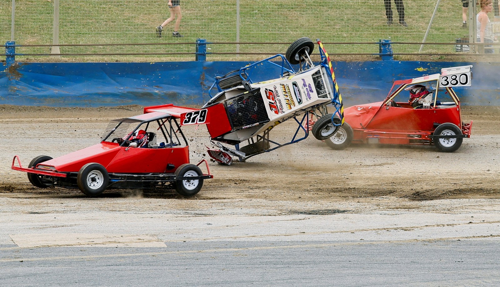 Several small cars race on a track, with one tumbling over and crashing.