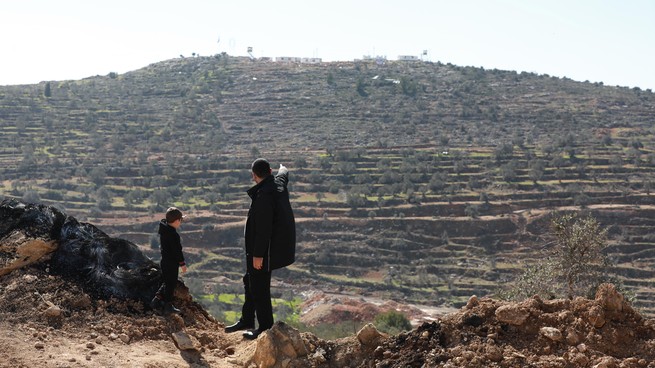 A man stands on a hillside with a young boy, pointing into the distance